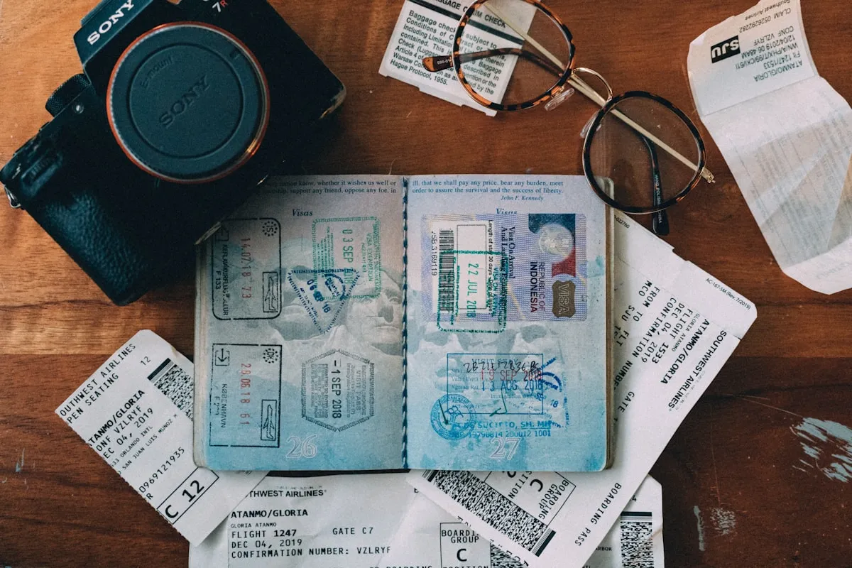 Open passport, travel documents and camera arranged on a desk